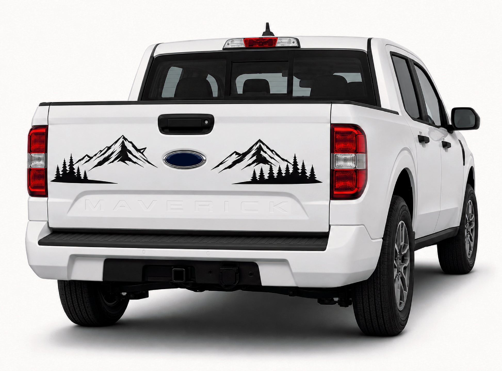 A white Ford Maverick pickup truck shown from the rear three-quarter angle on a light gray studio background, featuring a black mountain and pine tree decal across the tailgate above the embossed MAFERICK nameplate.