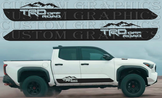 A white Toyota Tacoma pickup truck with a set of custom decals on the side, featuring a mountain design.