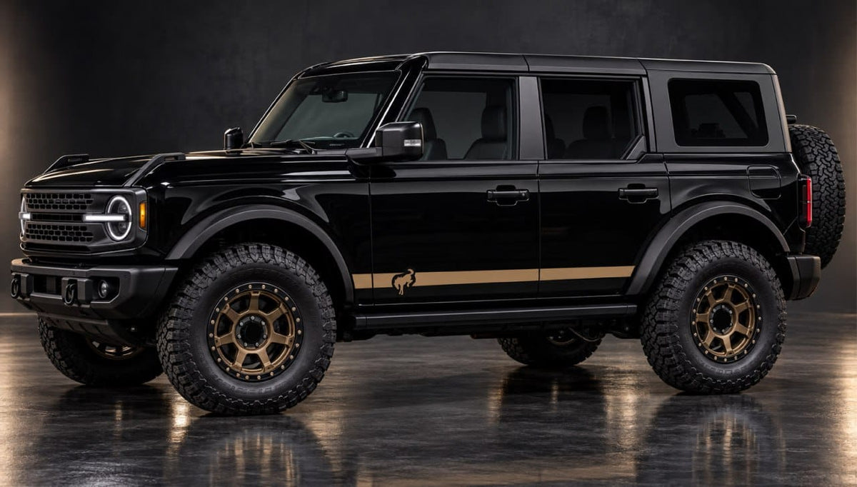 A black Ford Bronco with gold accents, including a side stripe and gold multi-spoke wheels, photographed in a dark studio setting.